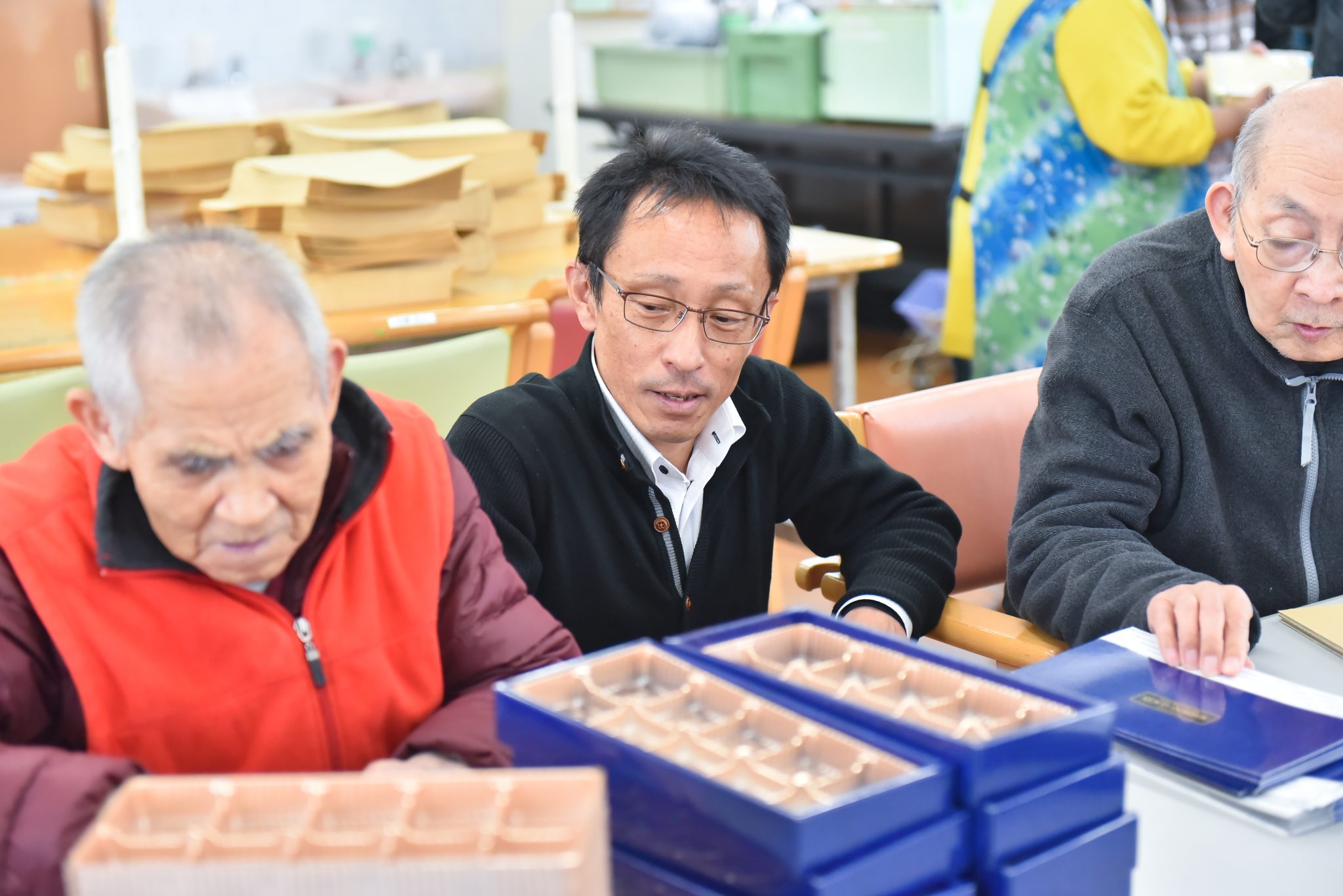入居者と職員が一緒に工芸作業を行っている様子。テーブルに材料が置かれている。