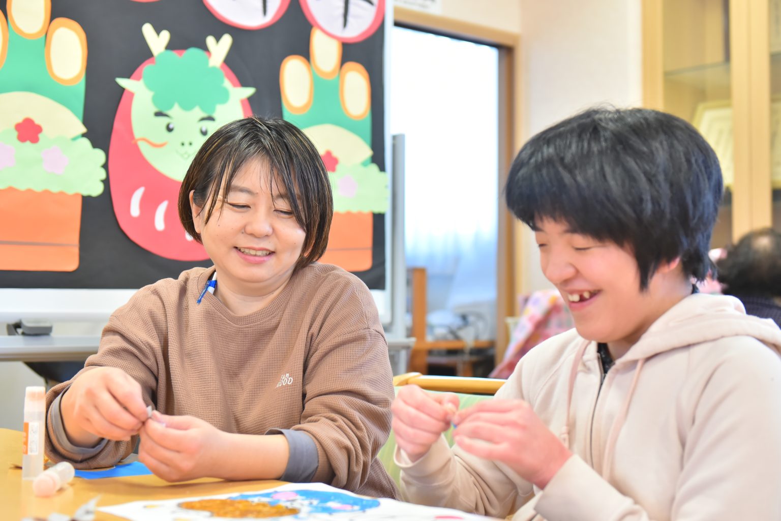 入居者がスタッフと一緒に工作活動を行っている。明るく和やかな雰囲気。